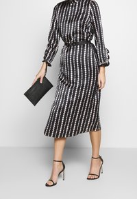 Vestido midi a rayas negras y rosas con mangas largas, cintura ceñida y puños con volantes. Acompañado de un bolso de mano negro y tacones con tiras.