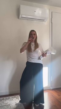 Femme debout à l'intérieur près d'une porte, tenant un objet emballé dans un bras et mettant quelque chose dans sa bouche avec l'autre main.