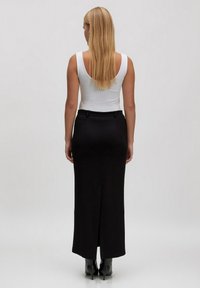 Schwarzer Bleistiftrock mit seitlichem Schlitz, aus glattem Stoff gefertigt. Verfügt über eine taillierte Passform und ein minimalistisches Design. Kombiniert mit einem weißen Tanktop.