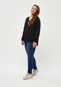 Schwarzes Langarmshirt mit weitem Ausschnitt, kombiniert mit blauen Jeans und beigen klobigen Sneakers. Schlichte, glatte Stoffqualität mit lässiger Passform.