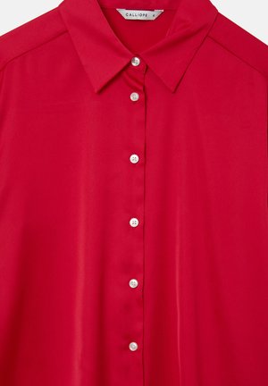 Blusa rossa realizzata in tessuto liscio con colletto classico, caratterizzata da bottoni bianchi al centro e un design delle spalle strutturato.