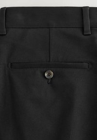 Dos d'un pantalon de costume noir avec une poche passepoilée boutonnée et des passants de ceinture visibles à la taille.