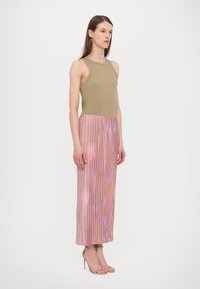 Beige ärmlös topp i kombination med en veckad rosa kjol med blommönster. Modellen bär neutrala sandalskor med remmar.