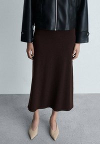 Braunen gestrickten Midirock kombiniert mit einer schwarzen, cropped Lederjacke und beigen spitzen Pumps. Glatte Textur, schlichtes Design.