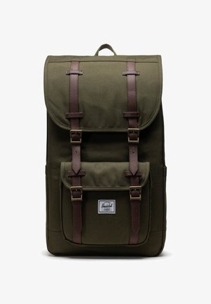 Olivengrøn canvas rygsæk med klap, brune læderstropper, frontlomme og et mærketikette. Har et håndtag på toppen for nem transport.