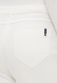 Hvit denim jeans med en subtil tekstur, en klassisk fem-lomme-design, og en liten marineblå og hvit stripet detalj på baklommen.
