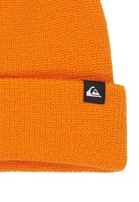 Orange knit beanie hat with a folded brim and a small black label featuring a white logo on the side. Textured material.