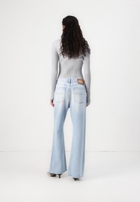 Jeans de pierna ancha azul claro con un acabado desvanecido y bolsillos traseros cosidos, combinados con un suéter ajustado de canalé gris.