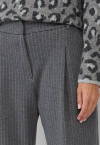 Grijze gestreepte broek van een textuurstof, met een voorplooien en een subtiele glans. De tailleband is recht en heeft geen zichtbare sluitingen.