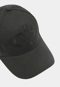 Gorra negra hecha de tela texturizada con un logo en relieve y un diseño floral, adornada con remaches decorativos en el panel frontal.