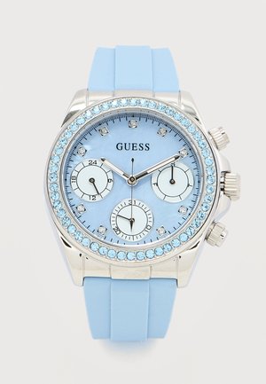 Montre-bracelet Guess bleu clair avec lunette ornée de cristaux, trois petits cadrans, aiguilles argentées et bracelet assorti bleu clair.
