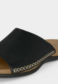 Μαύρο σανδάλι τύπου slip-on με παχύ επάνω μέρος, μπεζ αναπαυτική σόλα και διακοσμητικό λευκό σταυροβελονιά κατά μήκος της άκρης του επάνω μέρους.