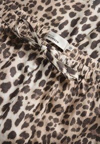 Leopardmønsteret stof med brune og beige nuancer, prydet med en snøre i taljen og en label, der læser "MAREN BY SIMONSEN."