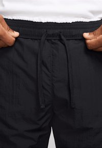 Pantalones cortos negros con cinturilla elástica y cierre de cordón. La tela ligera presenta una textura arrugada y un detalle de costura mínima.