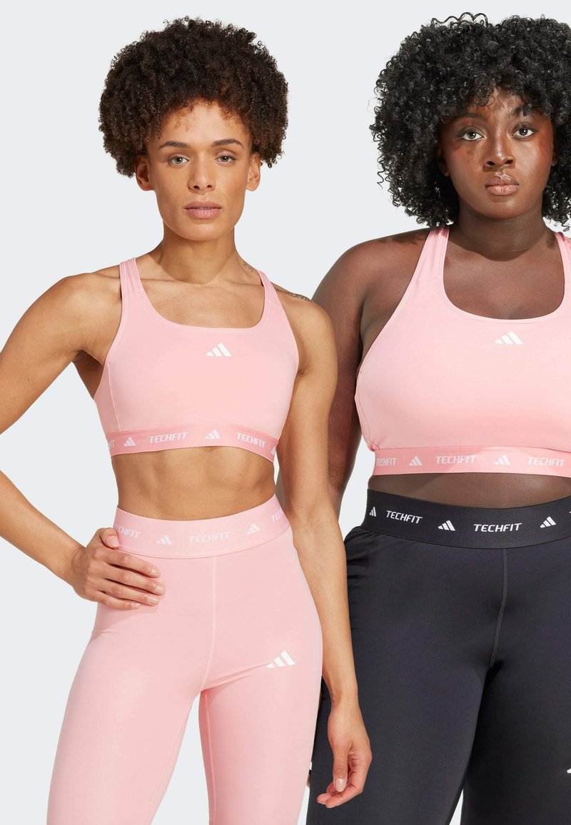 Dos modelos lucen atuendos deportivos: una lleva un sujetador deportivo rosa claro y leggings a juego; la otra lleva un sujetador deportivo oscuro y leggings.