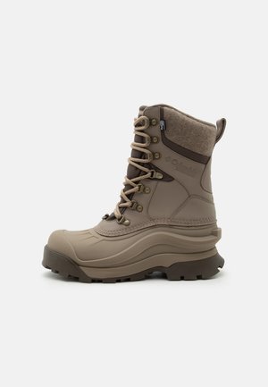 Botte d’hiver haute beige avec manchette rembourrée à la cheville, œillets métalliques, semelle épaisse et semelle robuste conçue pour un temps froid et enneigé.