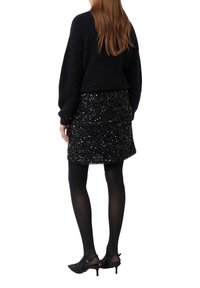 Schwarzer Strickpullover mit langen Ärmeln, kombiniert mit einem schwarzen Paillettenrock. Das Outfit umfasst schwarze Strumpfhosen und Absatzschuhe.