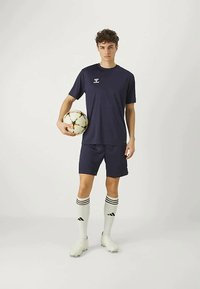 Marineblå idrettsdrakt med shorts og stripete hvite sokker. Spilleren holder en flerfarget fotball. Lett og atletisk passform.