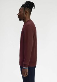Felpa bordeaux con scollo rotondo, polsini e orlo a costine. Presenta un piccolo logo sul petto. Tessuto liscio e texture.