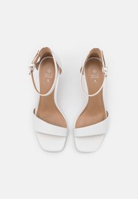 Sandales blanches à talons ouverts et design minimaliste, avec une large bride sur les orteils et une bride à la cheville avec une boucle. Matériau végétalien.