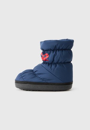 Botte en nylon matelassé bleu marine avec une semelle en caoutchouc noire. Présente un accent logo rouge vif sur le côté. Design court et arrondi.