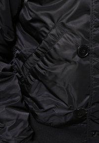 Schwarze Daunenjacke mit glatter, glänzender Textur, Knopfverschlüssen, geripptem Saum und einer Seitentasche mit gerafftem Material.