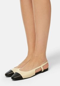 Ballerine in pelle beige con punta nera, design con tacco aperto e lati intagliati. Texture liscia con uno stile minimalista.