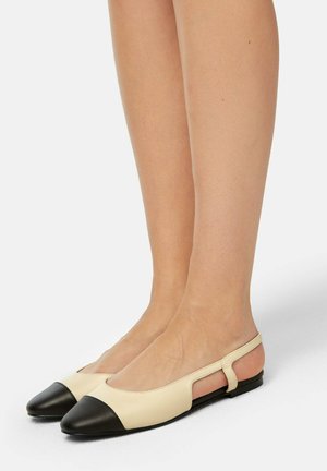 Ballerine in pelle beige con punta nera, design con tacco aperto e lati intagliati. Texture liscia con uno stile minimalista.