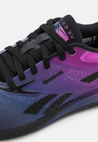 Reebok sneaker, amely színátmenetes purple és fekete dizájnnal rendelkezik, légáteresztő hálós felsőrésszel, strapabíró fűzőkkel és figyelemfelkeltő logóval.