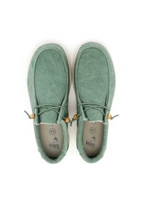 Zapatos de tela verdes tipo slip-on con forma redondeada, acentos decorativos de madera y suelas texturizadas al estilo espadrille.