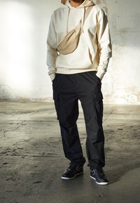 Beige mikina s kapucí a přední kapsou, černé cargo kalhoty s bočními kapsami a černé tenisky. Neformální outfit s kontrastem v barvách a materiálech.