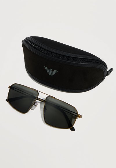 Μαύρα ορθογώνια γυαλιά ηλίου με λεπτά χρυσά πλαίσια δίπλα σε μαύρη θήκη με φερμουάρ που φέρει ασημένιο λογότυπο, σε λευκή επιφάνεια.