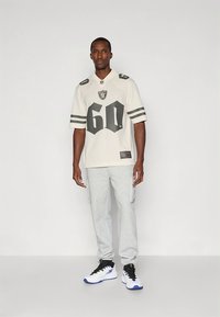 Fehér focimez szürke részletekkel és 60-as számmal. Világosszürke melegítőnadrággal és fekete-fehér sportcipőkkel kék részletekkel párosítva.