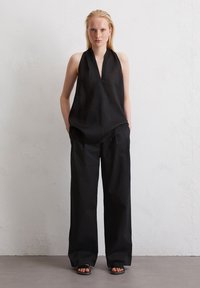 Haut noir à bretelles avec un décolleté en V plongeant, associé à un pantalon noir ample. Les deux en tissu léger, créant une apparence lisse et texturée.