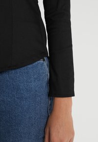 Svart långärmad topp med en figursydd design och rundad nederkant, matchad med blå denimjeans med en knappdetalj.