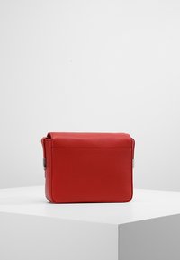 Rød læderhåndtaske med en struktureret overflade, rektangulær form, topflap og en lomme bagpå. Sølvfarvede hardwaredetaljer på siden.