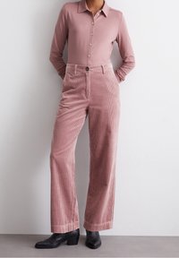 Långärmad rosa skjorta med knäppning, i kombination med högmidjade rosa kordbyxor. Byxorna har vida ben och en subtil randig struktur.