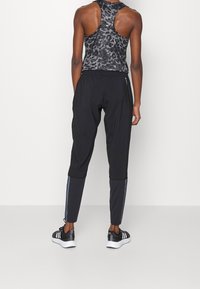 Svarta träningsbyxor med tapered design, elastisk midja och blå sidostråkar, matchade med en åtsittande svart leopardmönstrad tanktop.