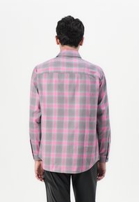 Camisa de franela gris con un patrón de cuadros en rosa y gris, de manga larga y con un cuello clásico. Se pueden ver detalles de botones en los puños.