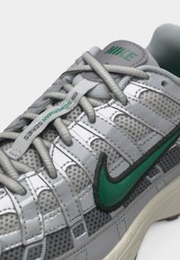 Baskets Nike grises avec logo Swoosh vert, superpositions réfléchissantes, empeigne en mesh respirant, et "III Bowman Series" imprimé sur l'étiquette des lacets.