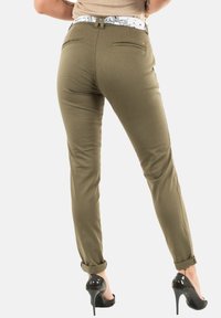 Olijfgroene broek met een witte patroon tailleband, slim fit ontwerp, achterzakken en omgeslagen boorden, gecombineerd met zwarte hoge hakken.