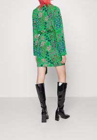 Zielona sukienka z wielokolorowymi wzorami florystycznymi i zwierzęcymi, posiada długie rękawy i pasek. Noszona z błyszczącymi czarnymi botkami do kolan.