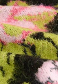 Tissu tricoté doux et duveteux avec des motifs abstraits roses, verts, noirs et violets clairs, présenté en gros plan sur les plis et les détails de texture.