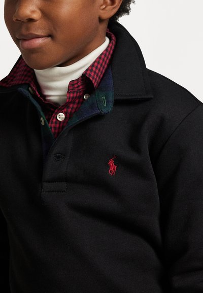 Črna polo majica z rdečim vezenim logotipom, prekrita z rdečo in črno karirano srajco, pod katero je bela turtleneck majica.