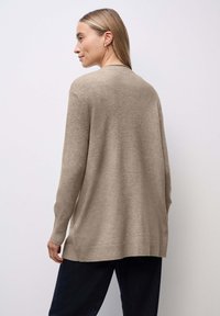 Cárdigan de punto beige con un corte relajado, cuello redondo y puños y dobladillo de canalé, con costuras mínimas y una textura suave.