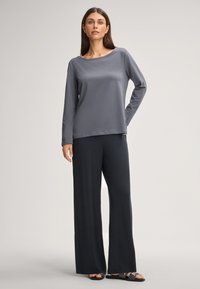 Šedé dlouhé rukávy s černými volnými kalhotami. Hladká tkanina, uvolněný střih a decentní detail výstřihu. Minimální akcenty na sandálech.