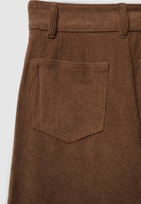 Gros plan sur une jupe en velours côtelé marron montrant la poche arrière, les passants de ceinture et la texture côtelée verticale.