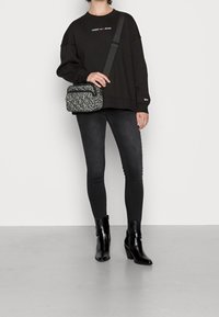 Persona che indossa un felpa nera Tommy Jeans, jeans skinny scuri, stivaletti neri con tacco alla caviglia e porta una borsa a tracolla grigia con stampa leopardata.