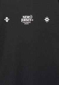 Sort bomuld t-shirt med hvid broderi. Centreret tekst lyder "NEW JERSEY THE GARDEN STATE" med et dekorativt emblem og en stjerne på hver side.
