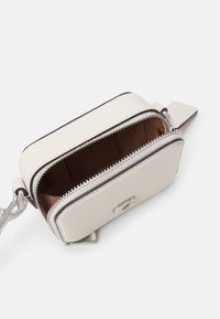 Compact pouch in pelle crema con zip e dettagli in argento, caratterizzata da una superficie testurizzata e un interno marrone. La zip aperta rivela l'interno.